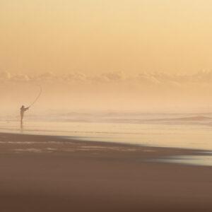 Pêcheur solitaire sur la plage sous un horizon de brume et de nuages