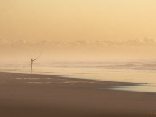 Pêcheur solitaire sur la plage sous un horizon de brume et de nuages