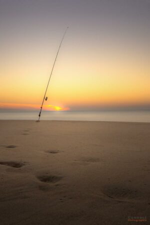 Plénitude et sérénité avec cette canne à pêche planté sur la plage au coucher du soleil au bord de l'océan